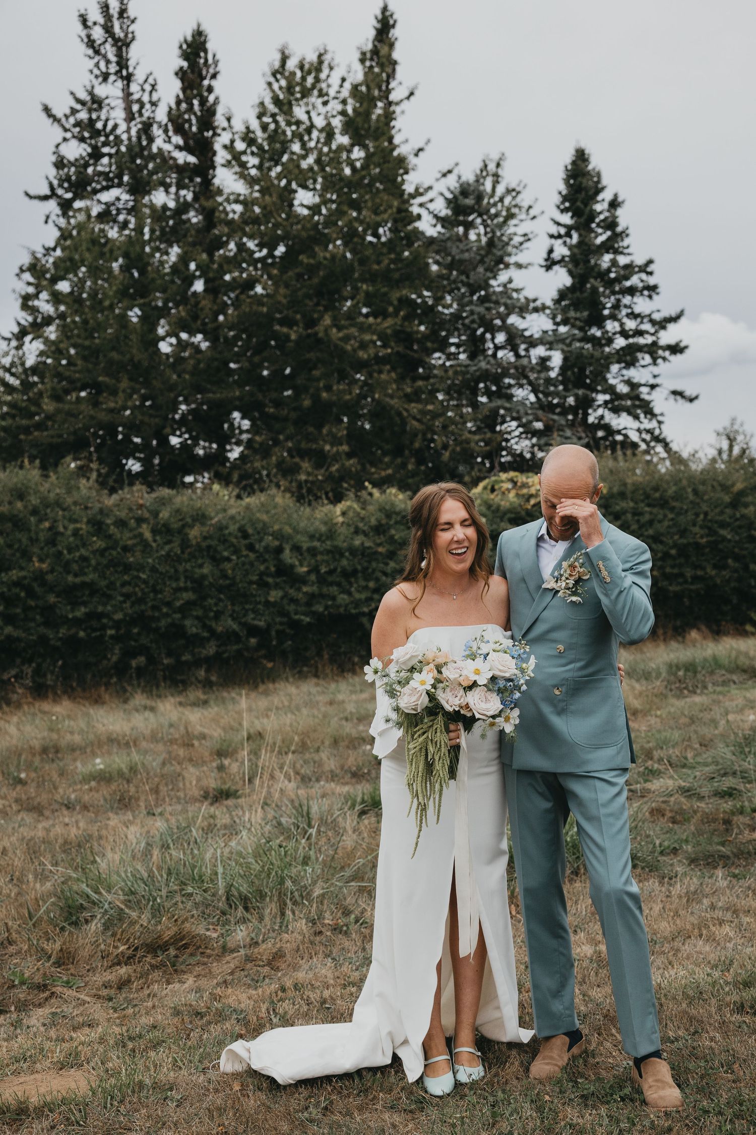A wedding couple poses against a backdrop of evergreen trees on their special day.