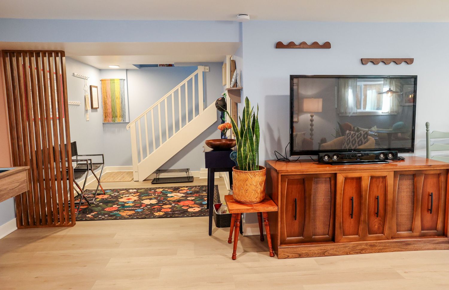 Modern basement entertainment area with wooden media console and slatted room divider.