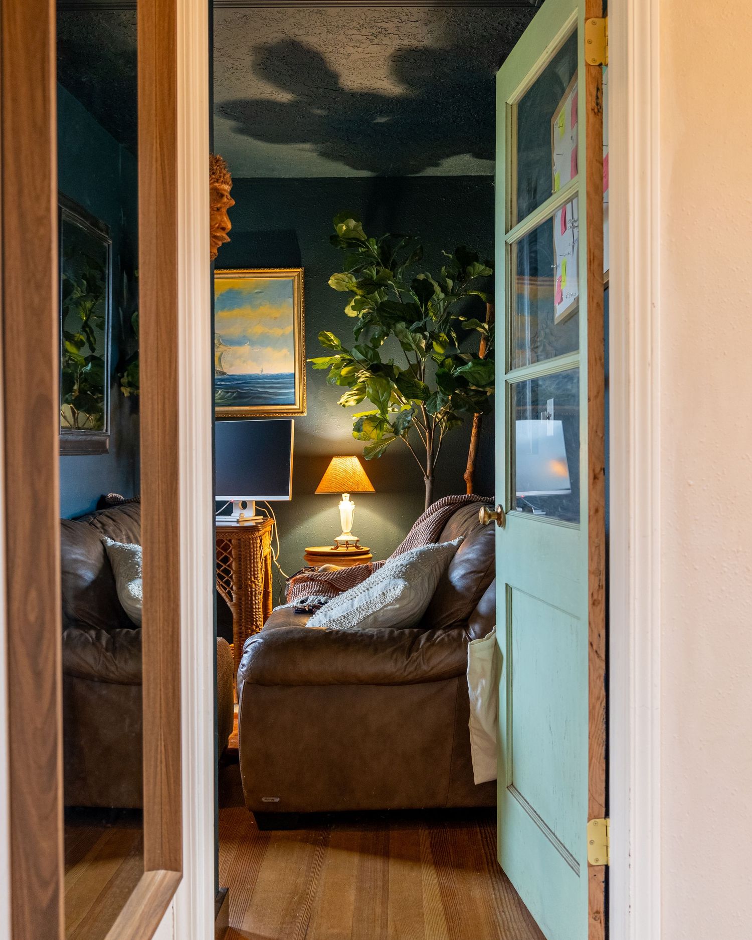 Moody interior doorway with turquoise door frame leading to room with brown leather sofa and artwork.