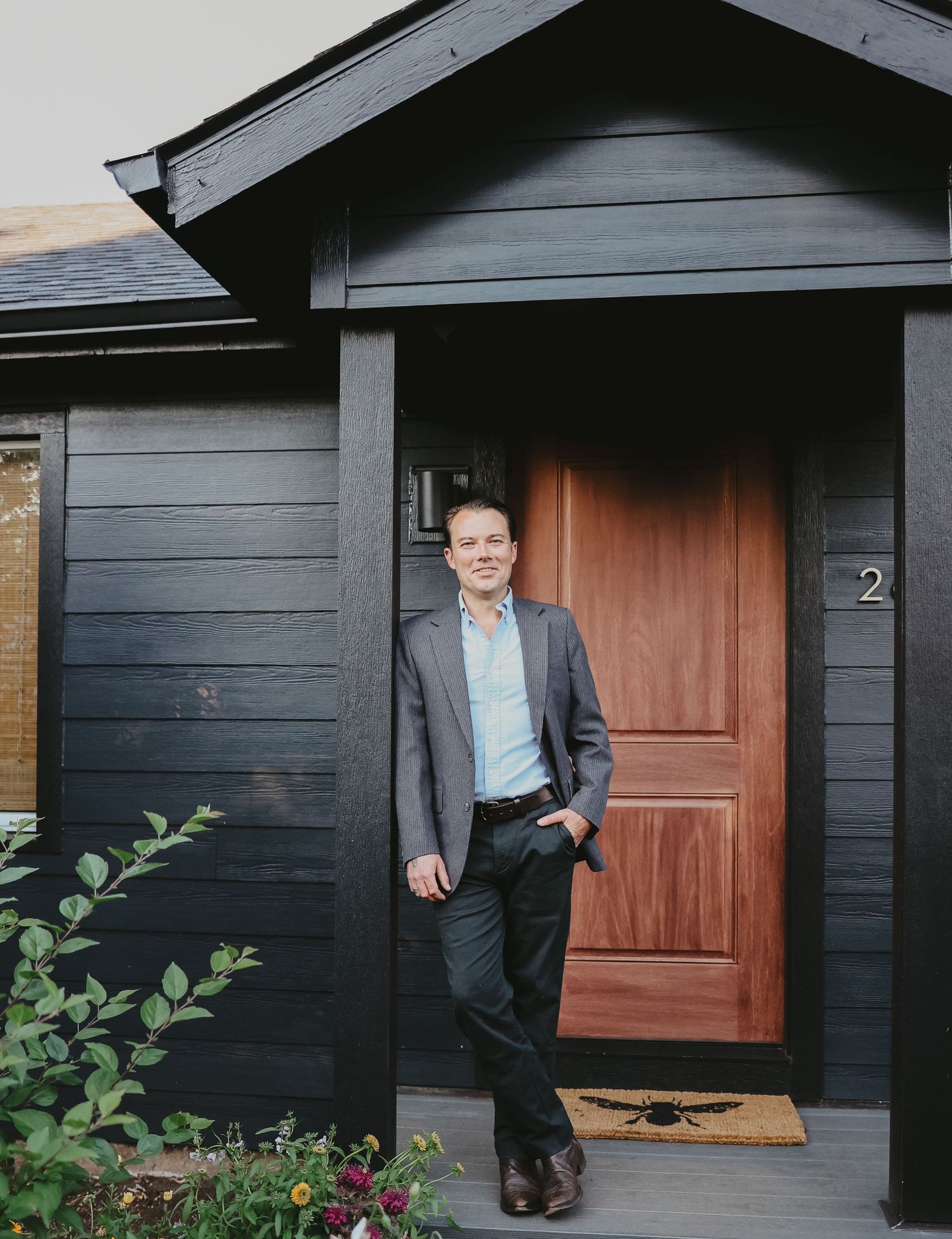 A modern black house exterior with a wooden red door and welcome mat on the front porch.