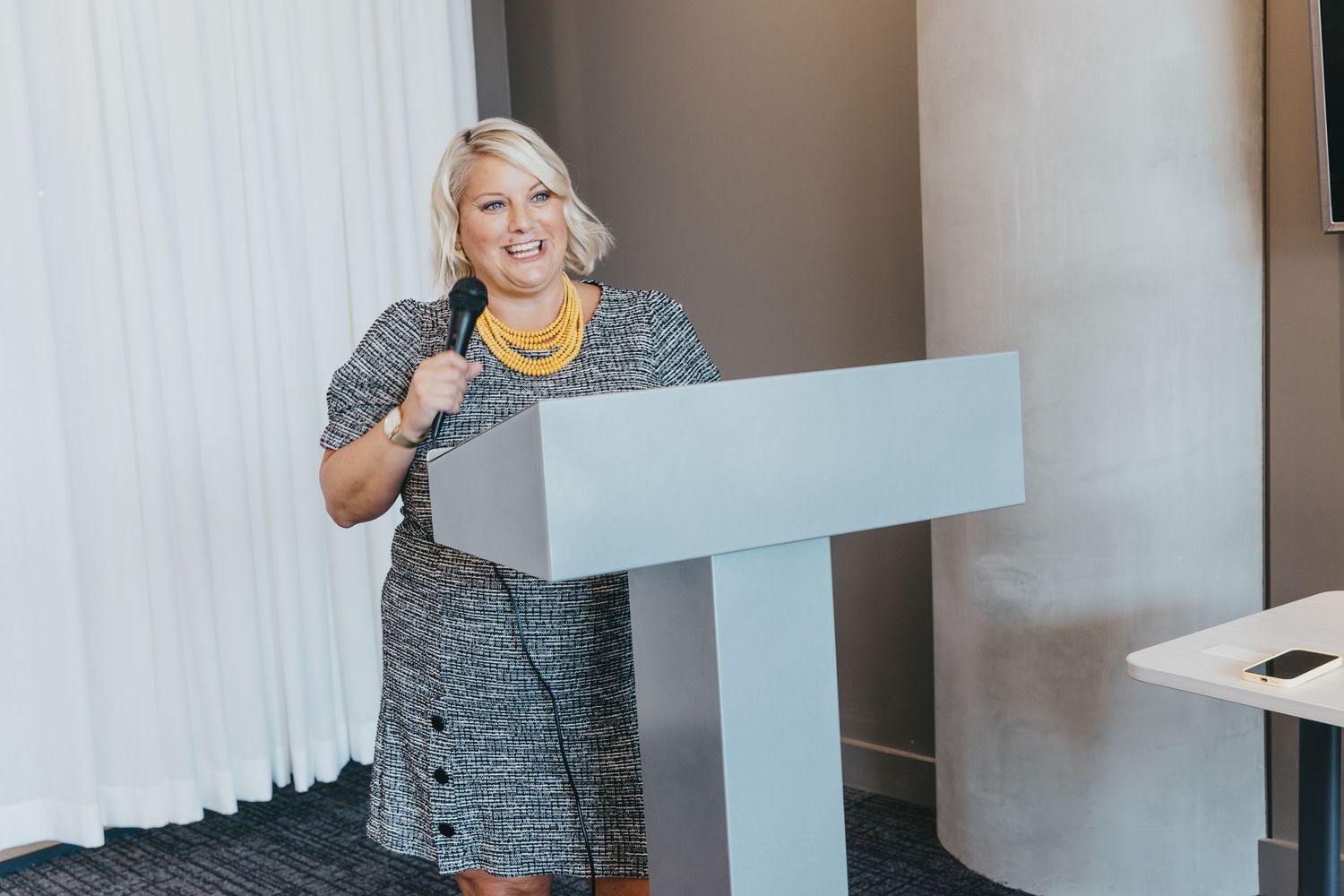 A person in business attire gestures while giving a presentation in a professional office setting.
