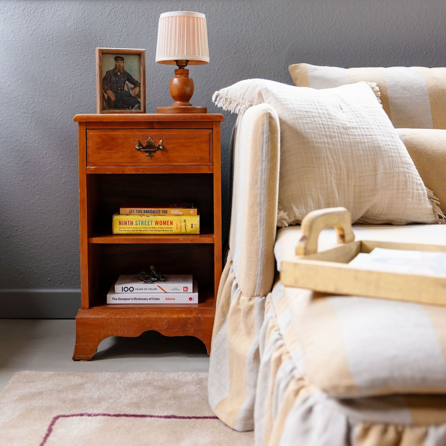 Wooden bedside table with orange lamp and cream colored sofa with throw pillows.
