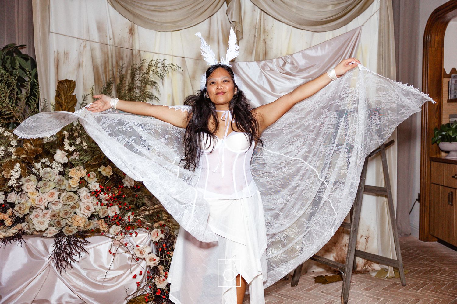 A young girl in a white dress twirls and dances with flowing sheer curtains in a sunlit room.