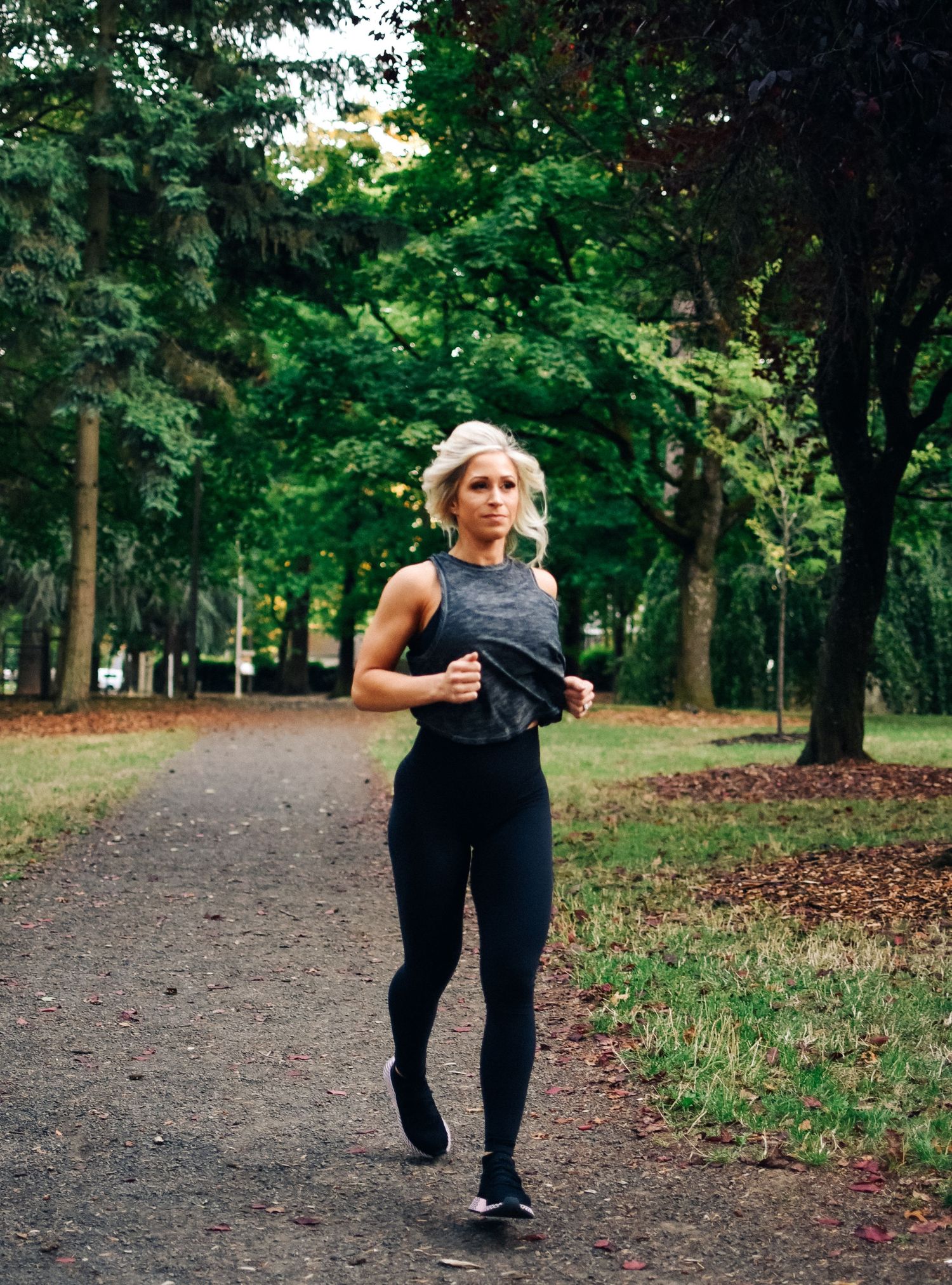 Person jogging on tree-lined park path wearing dark athletic wear.
