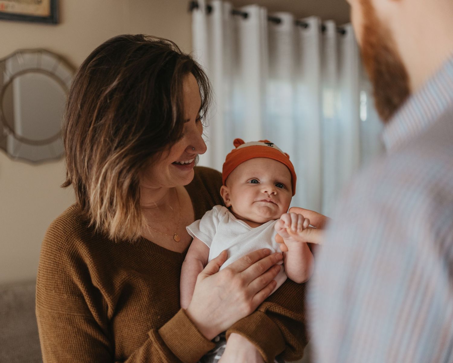 Intimate indoor portrait of parents with newborn baby in warm lighting.