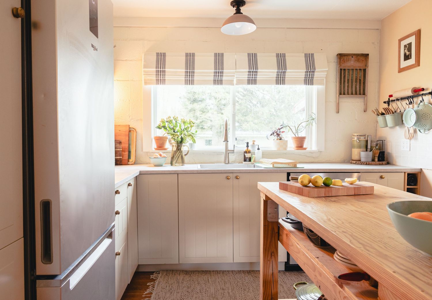 Modern white kitchen with wooden countertops, striped Roman shade, and natural light from window above sink.