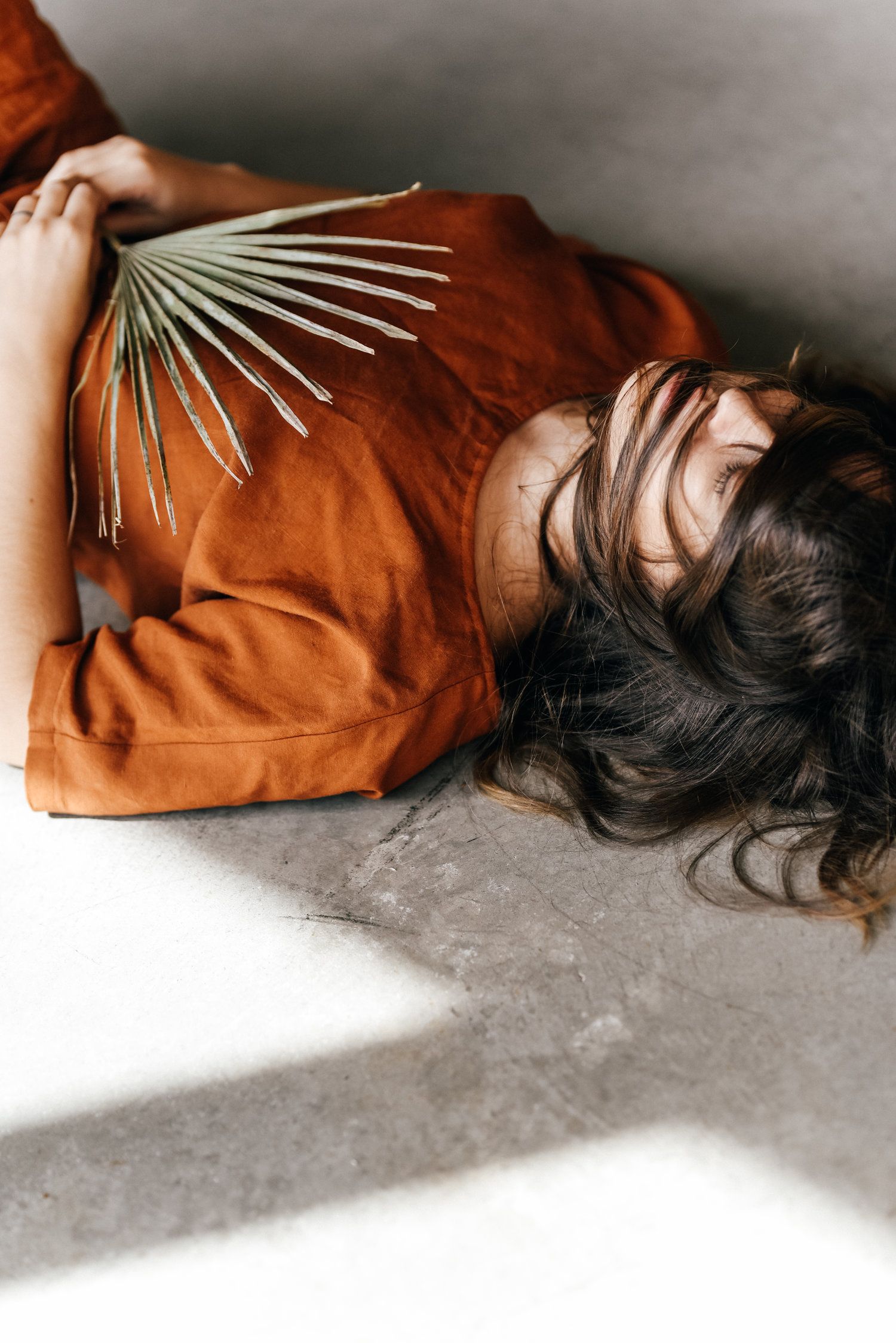 Artistic portrait on floor wearing orange top with palm leaf decoration in dramatic lighting.