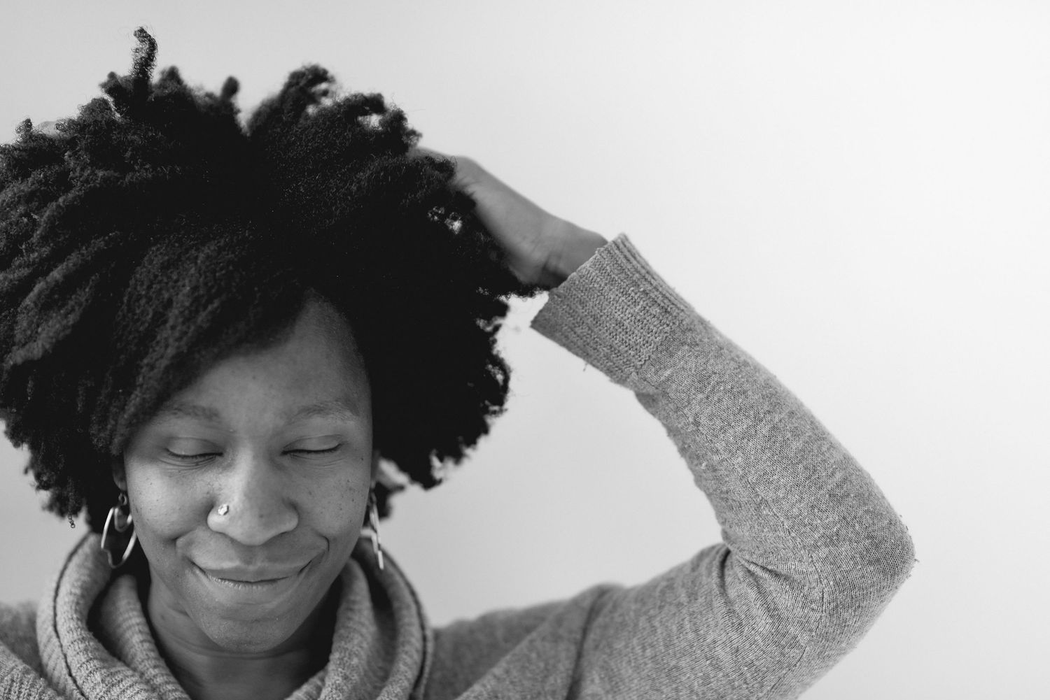 Black and white portrait of person with natural hair touching head and smiling.