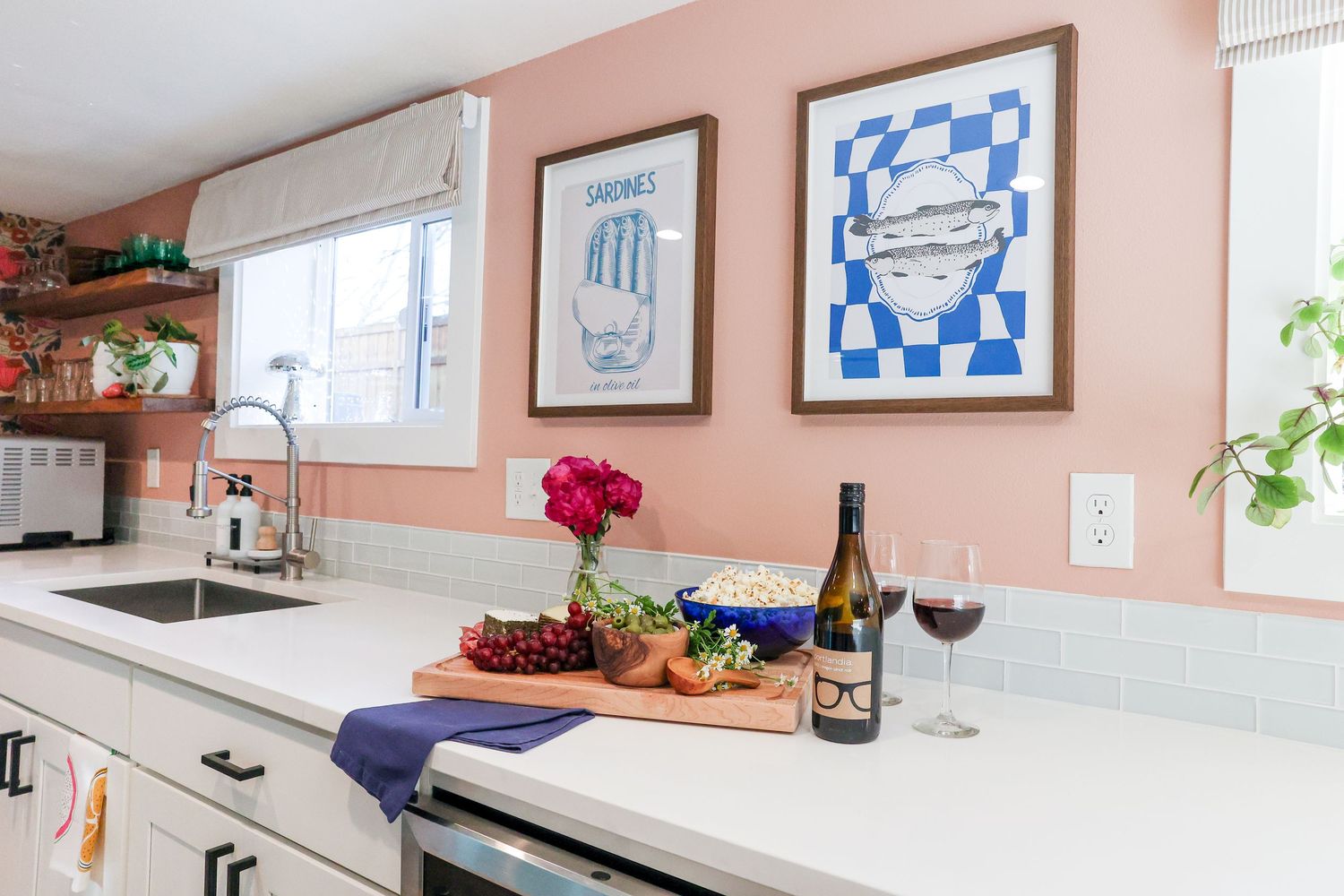 Kitchen counter with wine, cheese board, and blue artwork against salmon-colored walls.