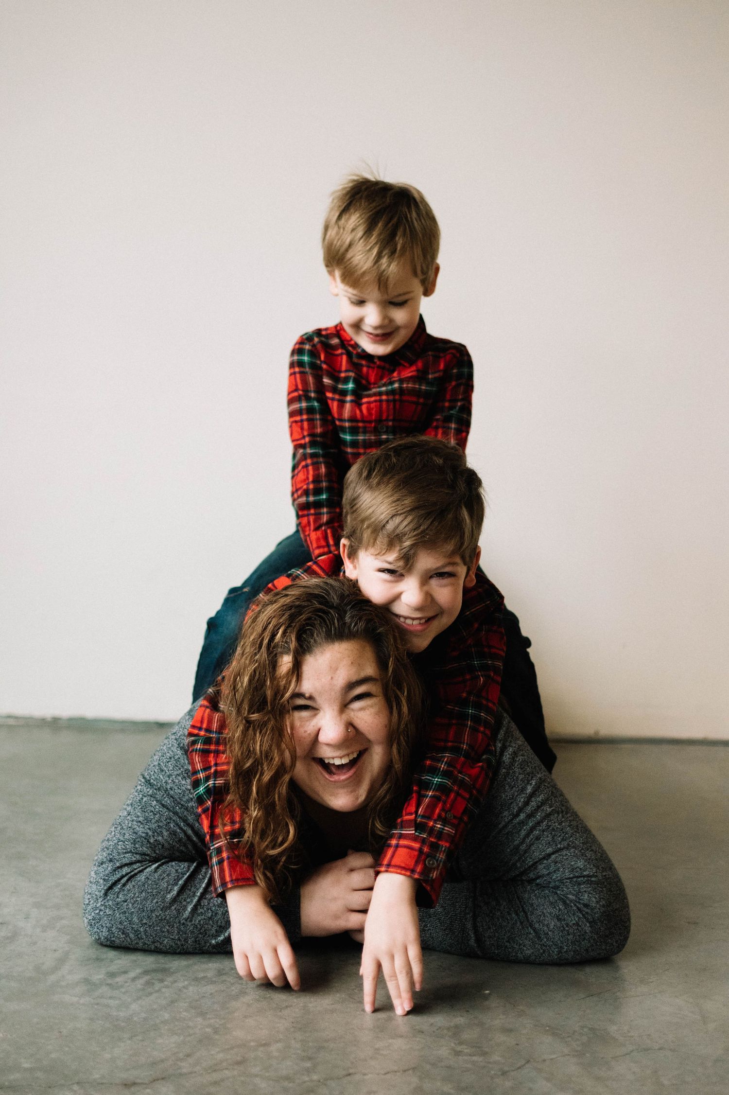Playful family pile-up wearing matching red plaid shirts on gray background.