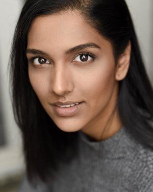 Close up headshot of a person with long dark hair and warm smile against a neutral background.