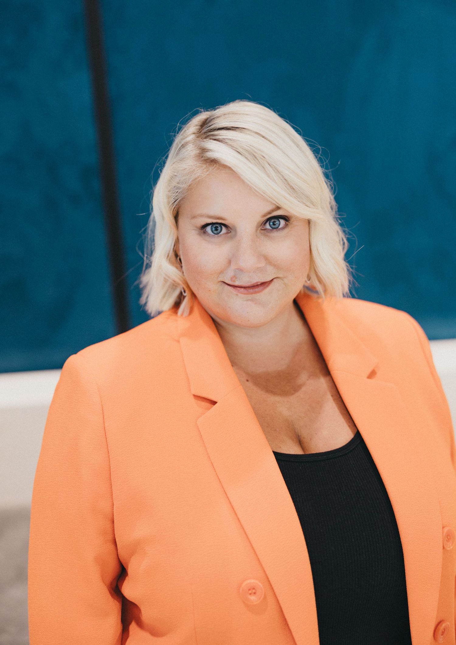 Professional portrait of person wearing vibrant coral blazer against blue background.