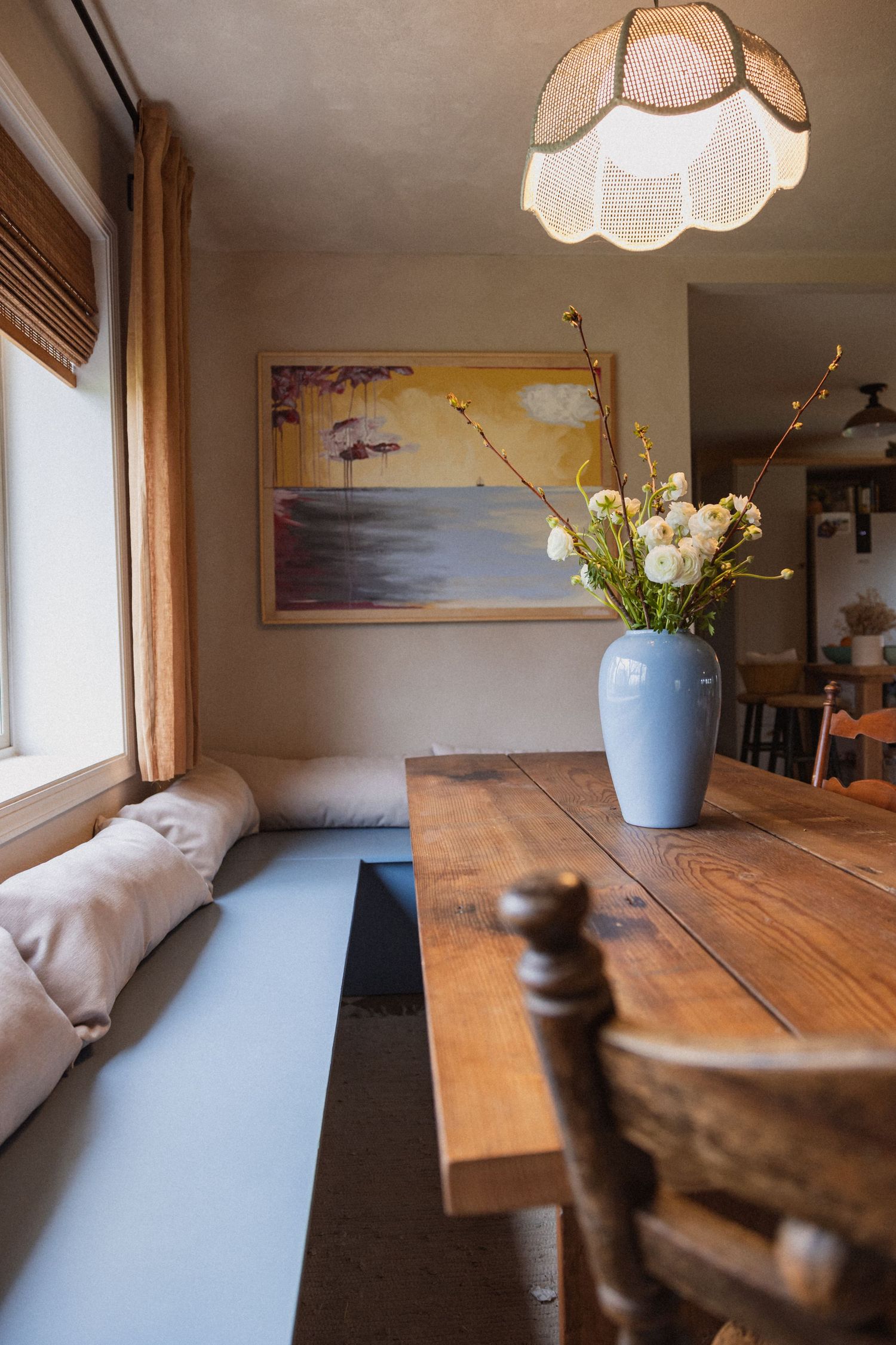 Cozy dining nook with wooden table, pendant lamp, and landscape artwork on wall.