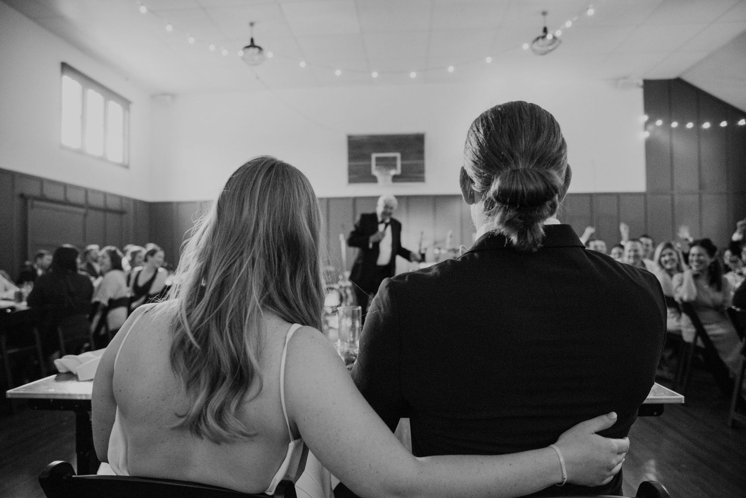 Black and white photo of guests watching an event in a gymnasium setting.