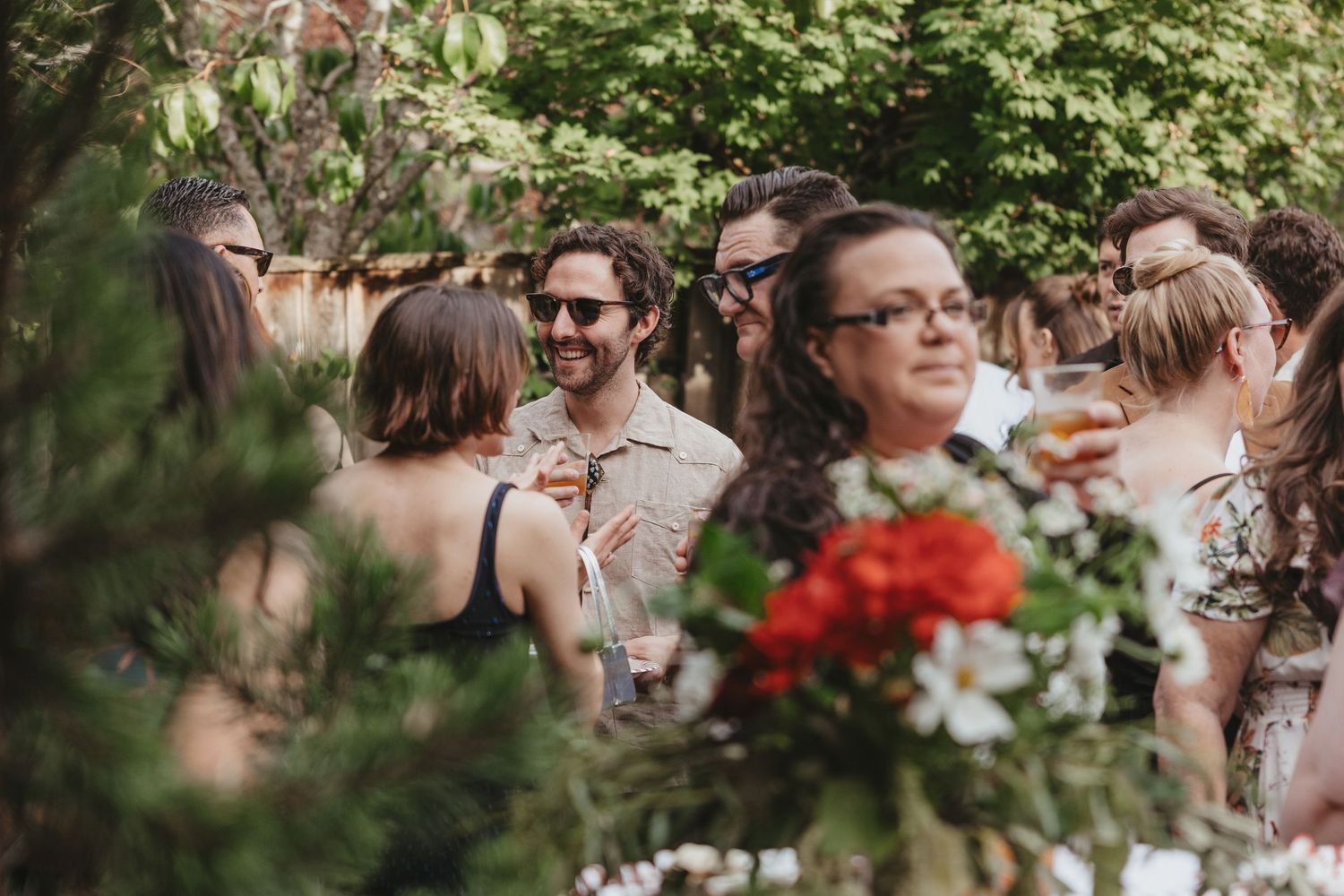 Wedding celebration in a lush garden setting with guests mingling under green foliage.