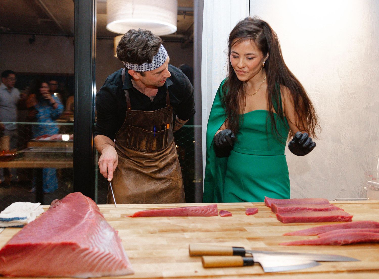People working together in a commercial kitchen space preparing food on a large wooden countertop.