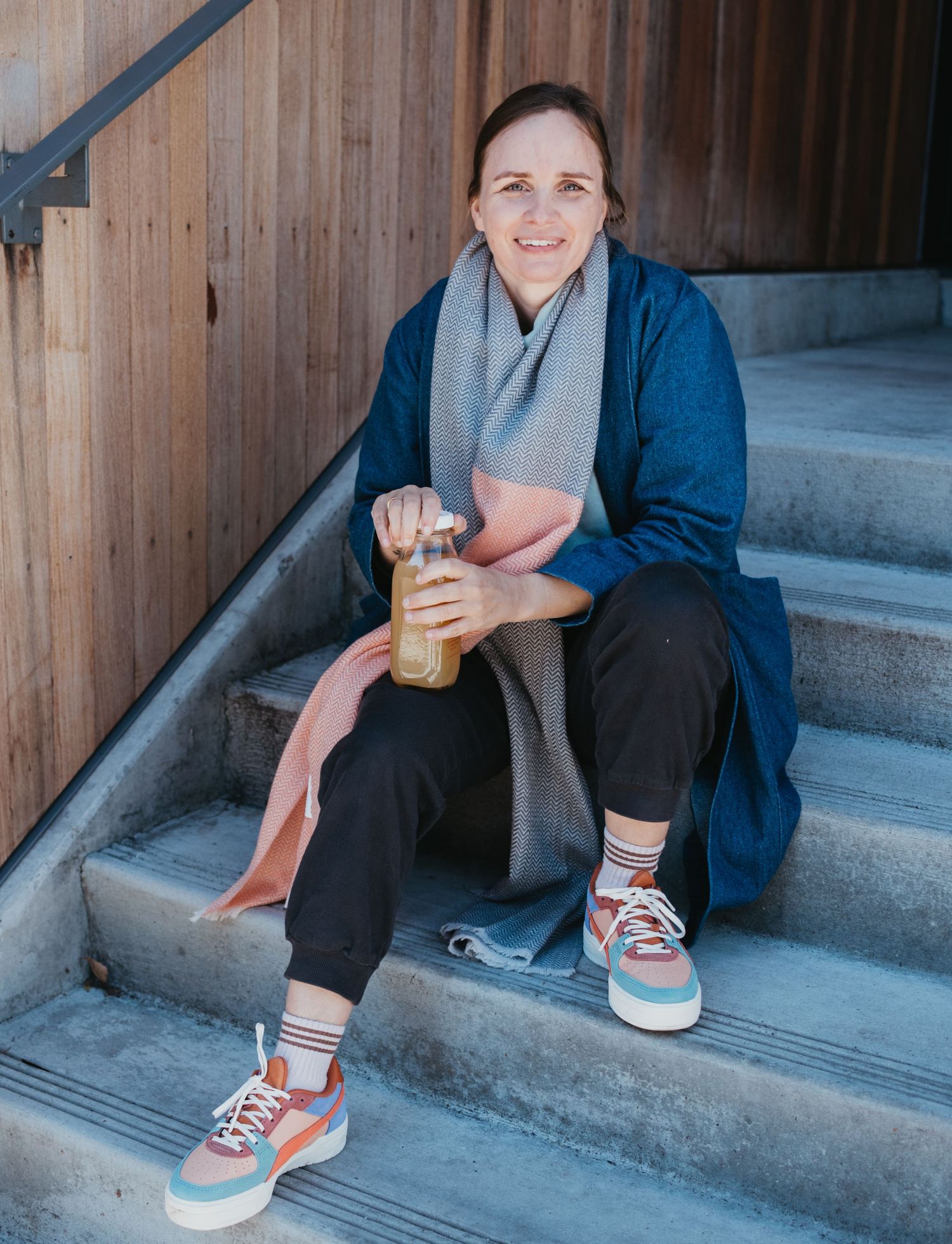 A person wearing blue jeans and colorful sneakers sits on concrete steps in a casual pose.