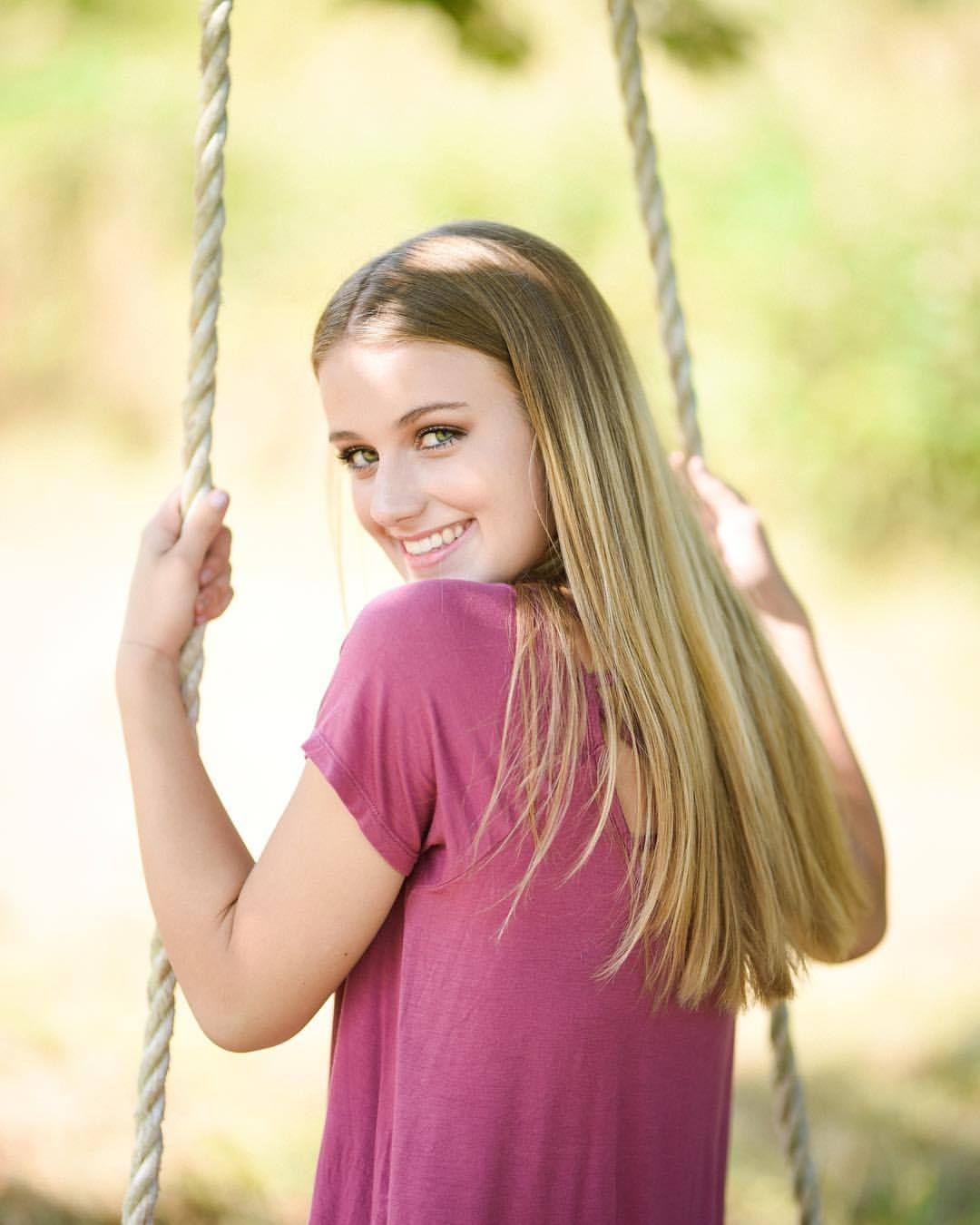 Portrait of someone on a rope swing wearing a burgundy shirt with long blonde hair.
