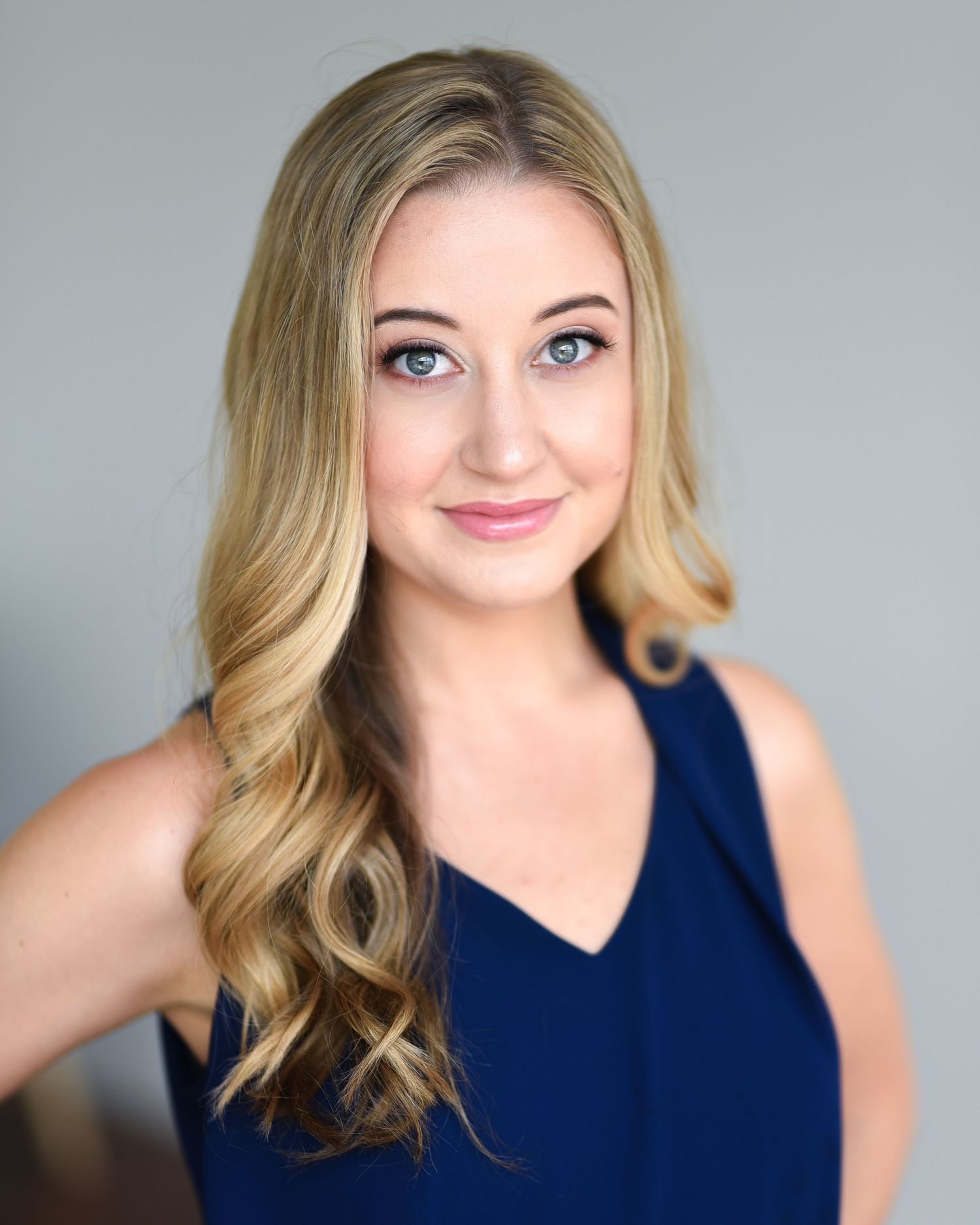 Professional headshot in a navy blue sleeveless top against a grey background.