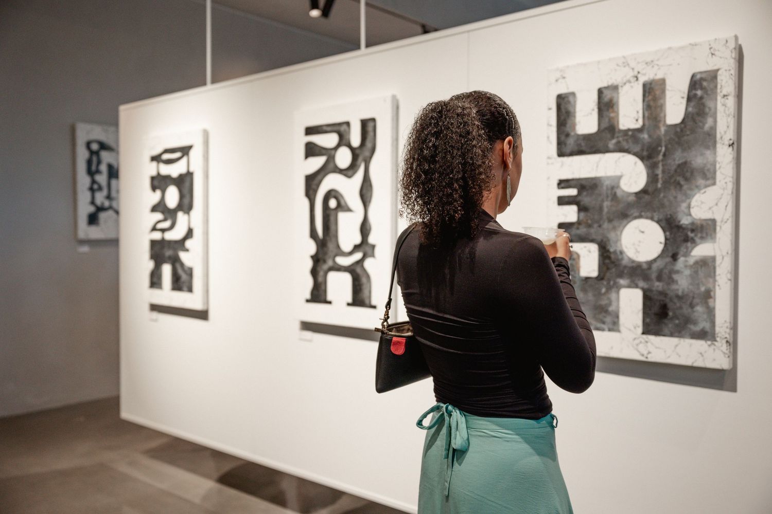 A visitor examines black and white artwork displayed in a gallery with white walls and track lighting.