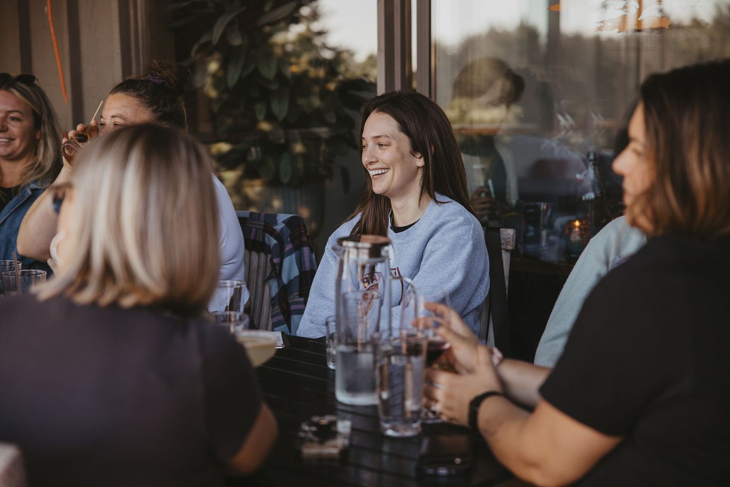 Friends gather around a table enjoying drinks and laughter at a restaurant during golden hour.