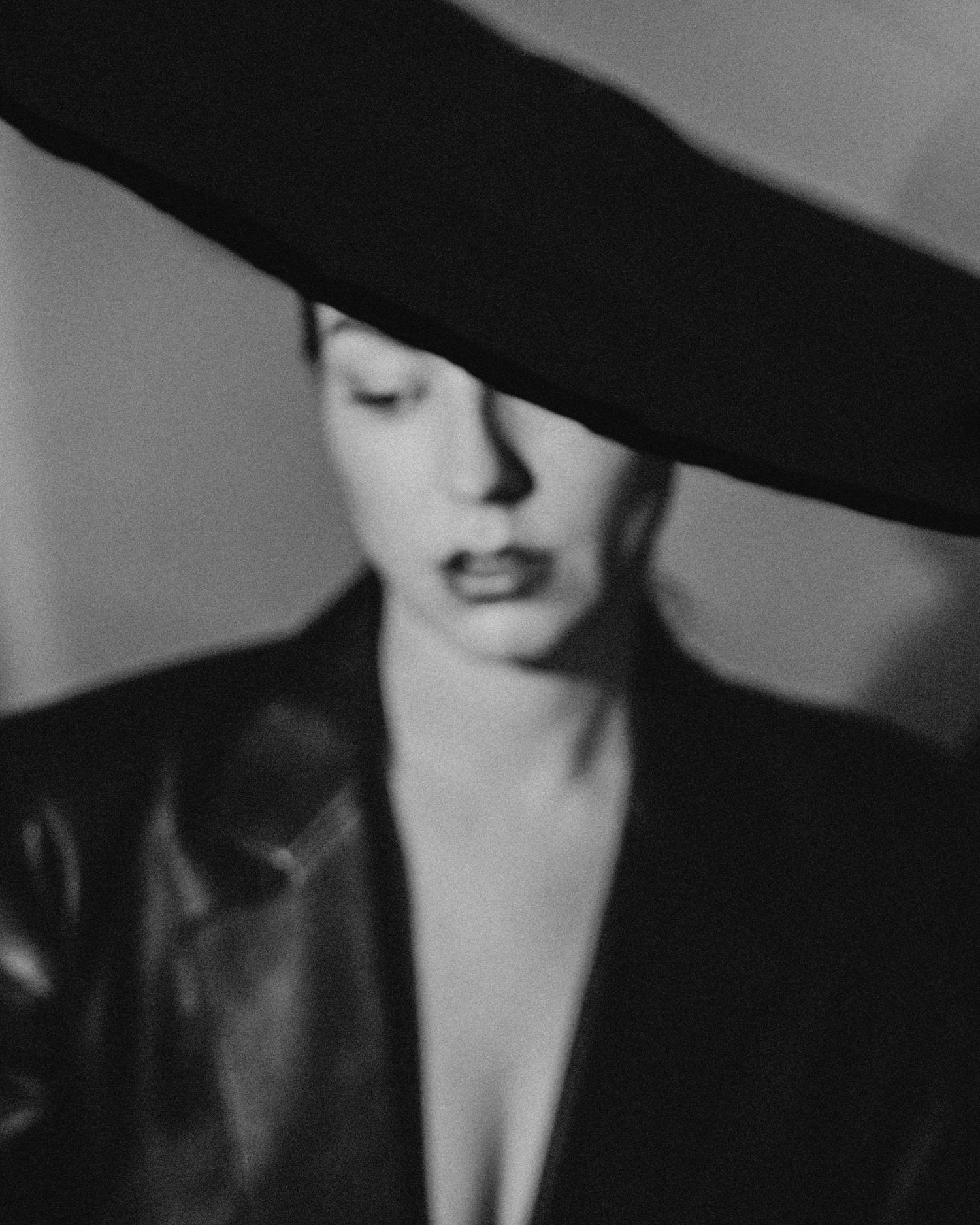 A black and white artistic portrait showing someone wearing a wide-brimmed hat with dramatic lighting and shadows.
