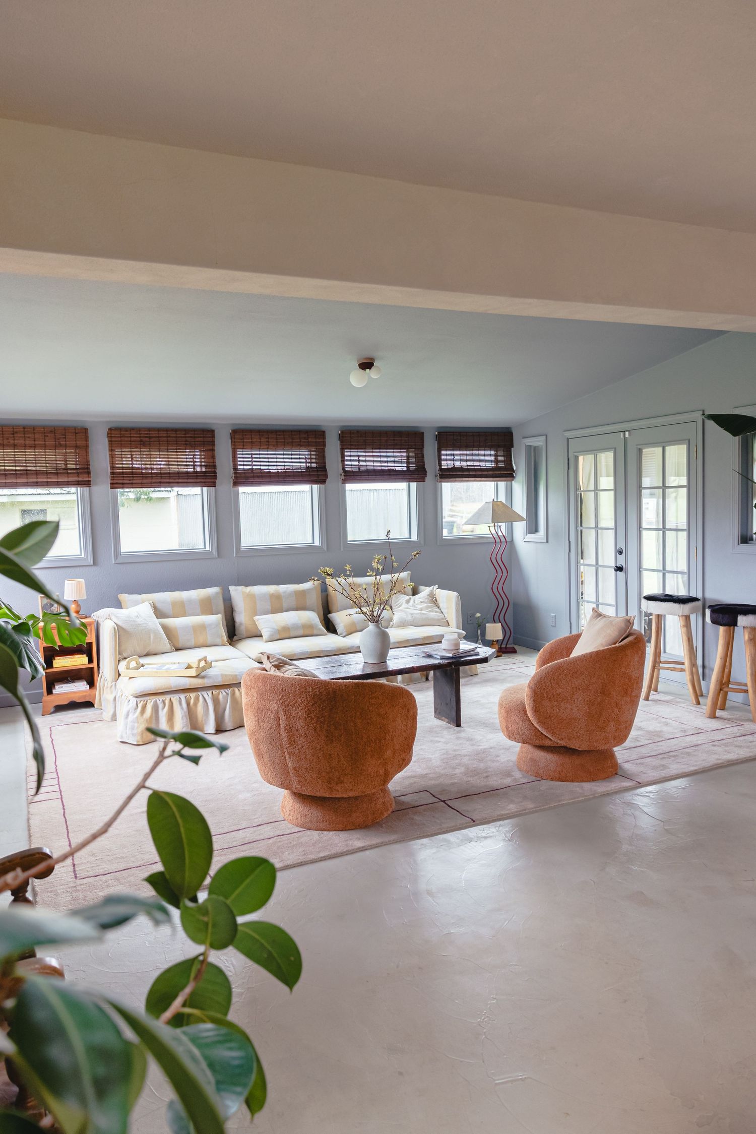 Bright living room with curved chairs, concrete floors and bamboo window shades.