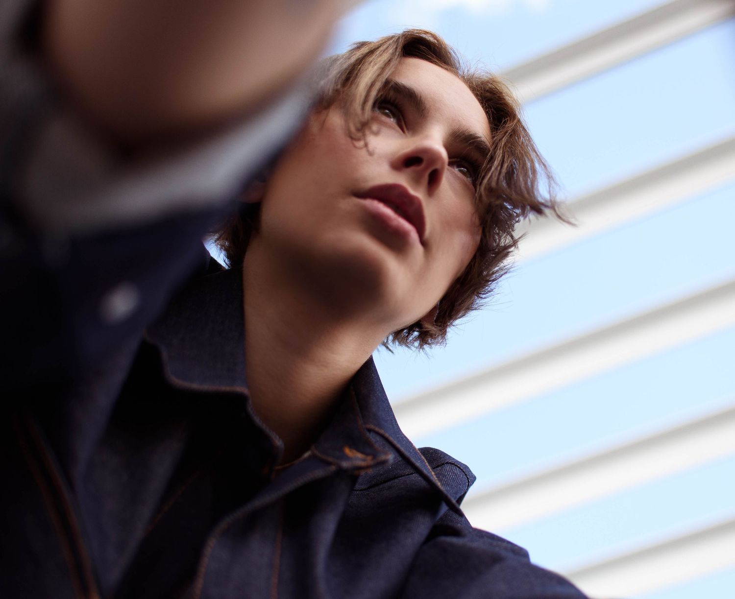 Dramatic low angle portrait of person in dark clothing against sky.