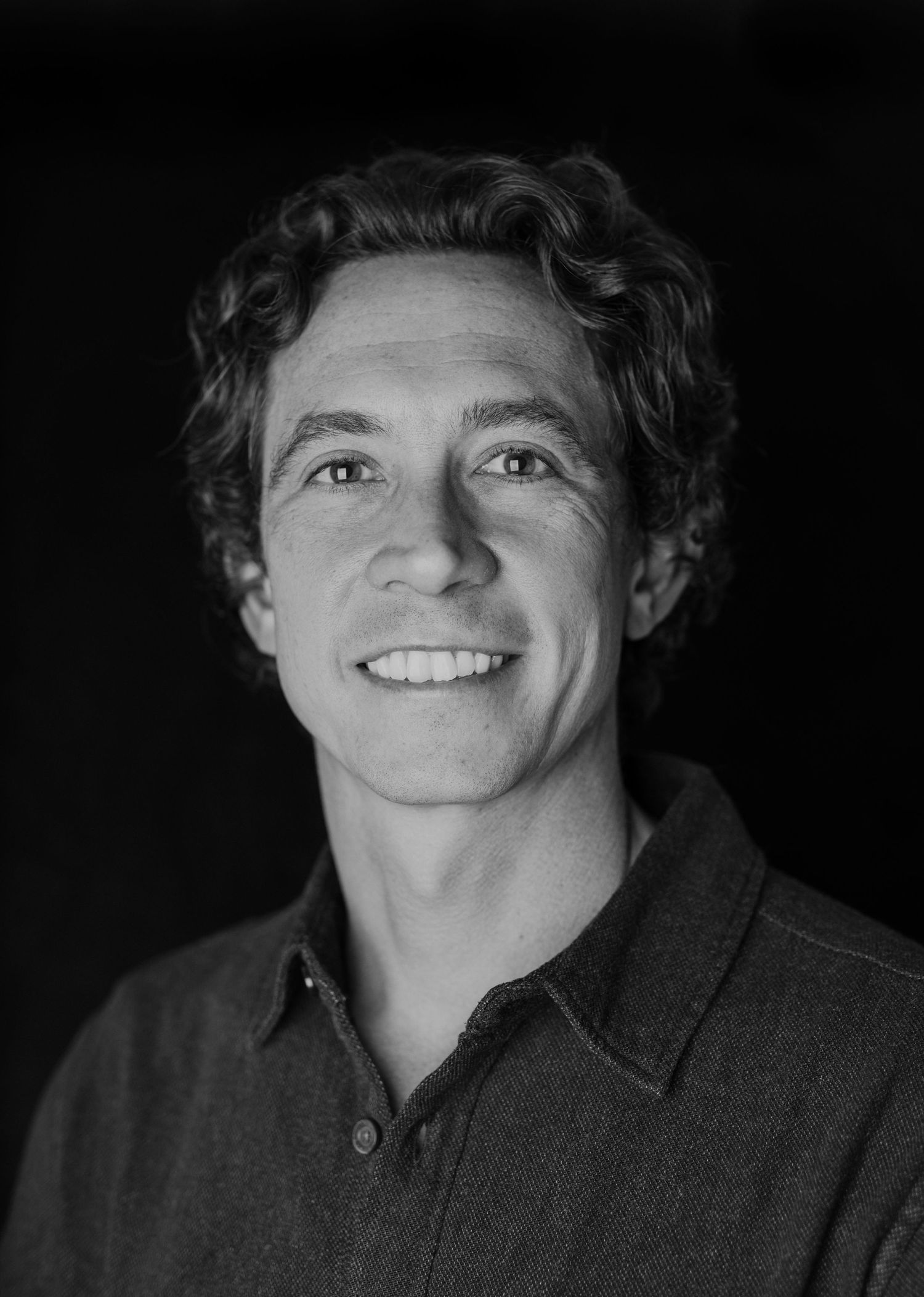 Black and white portrait of a person with curly hair wearing a collared shirt.
