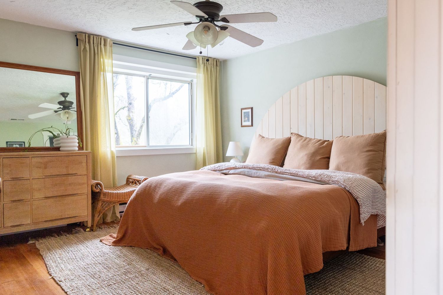 Bright bedroom with vintage-style cream headboard, terracotta bedding, and wooden dresser.