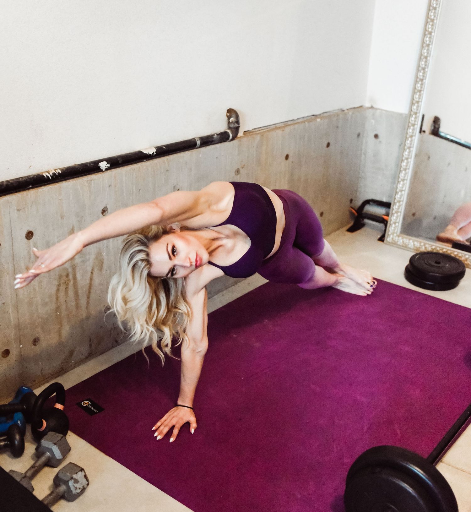 Person performing side plank exercise on purple yoga mat with weights nearby.
