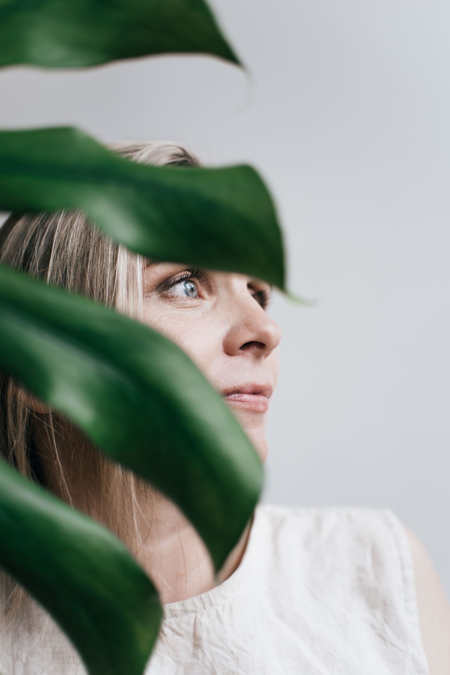 Artistic portrait peeking through green tropical leaves against white background.