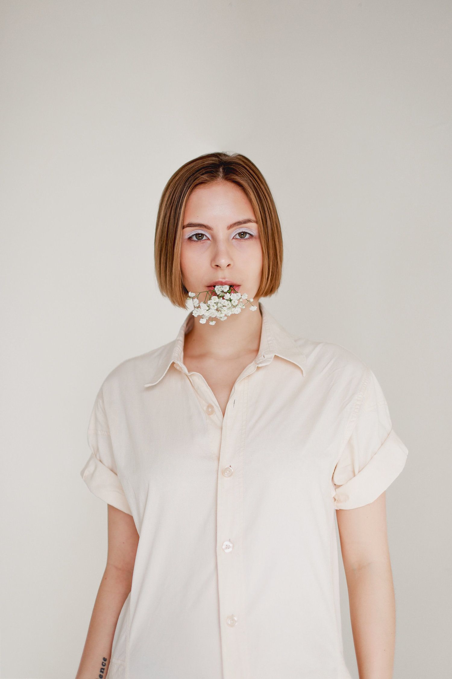 Minimalist fashion portrait with white button-down shirt and floral neck decoration.