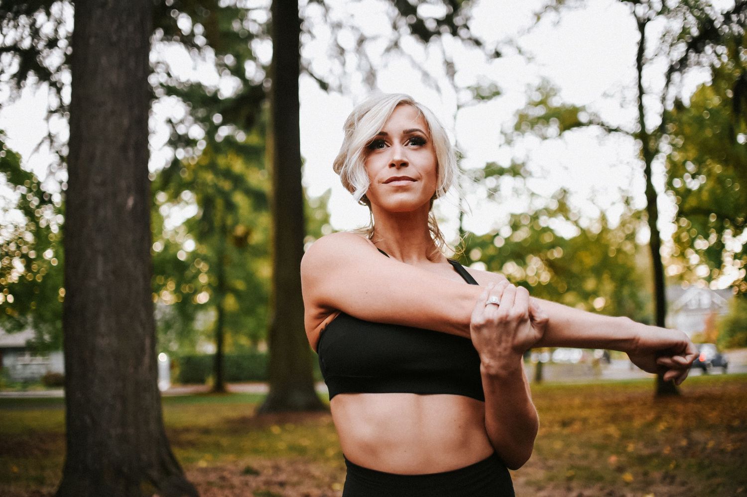 Person stretching arms in park wearing black athletic wear during autumn season.