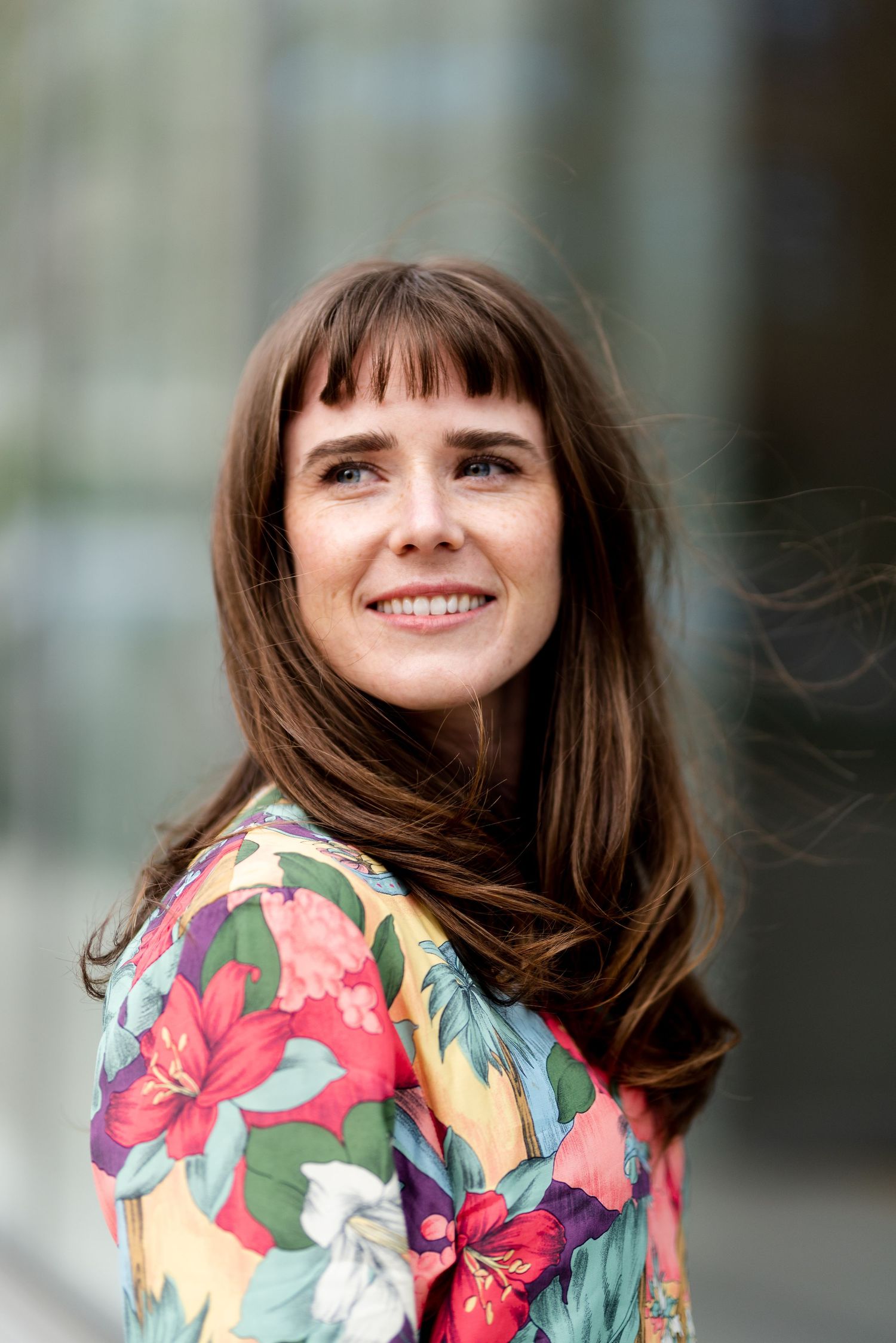 Professional portrait of a person in a colorful floral top smiling warmly against a blurred background.