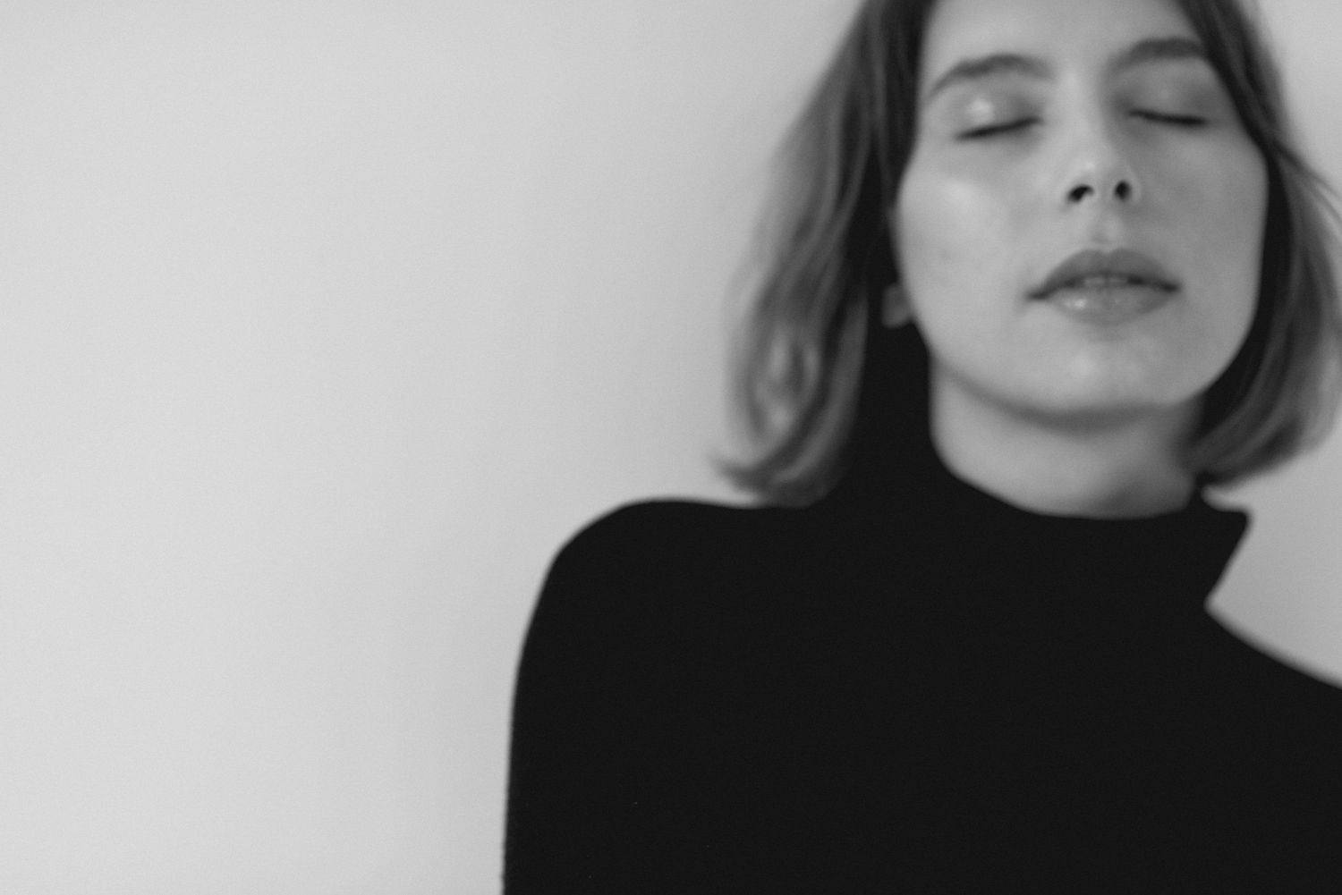Moody black and white portrait in turtleneck against white background.