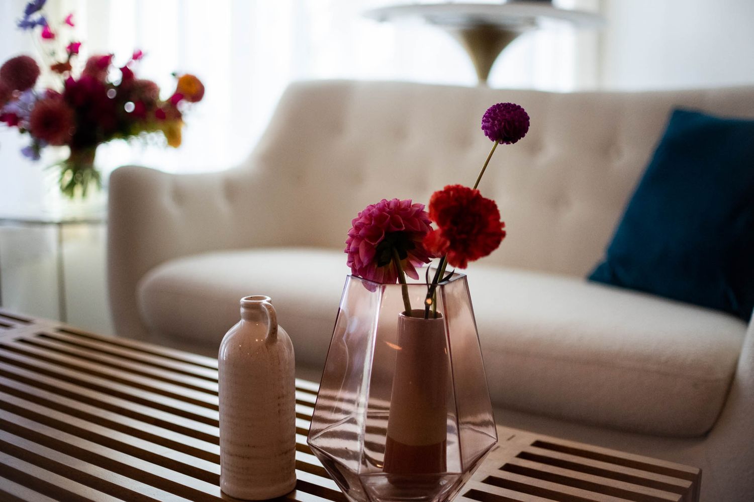 Close-up of deep red flowers in vases on coffee table with beige sofa in background.