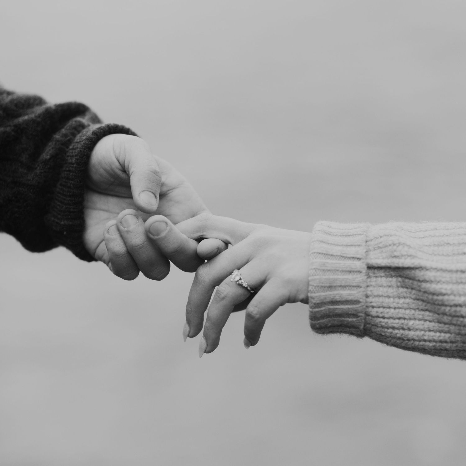 Close-up black and white photo of two hands with engagement rings touching.