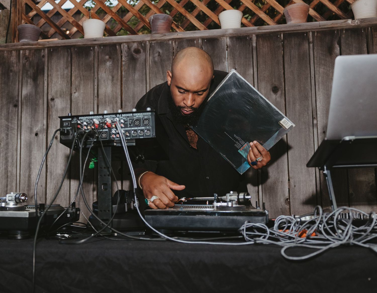 DJ performs at a live event using electronic equipment and mixers on a wooden table setup.
