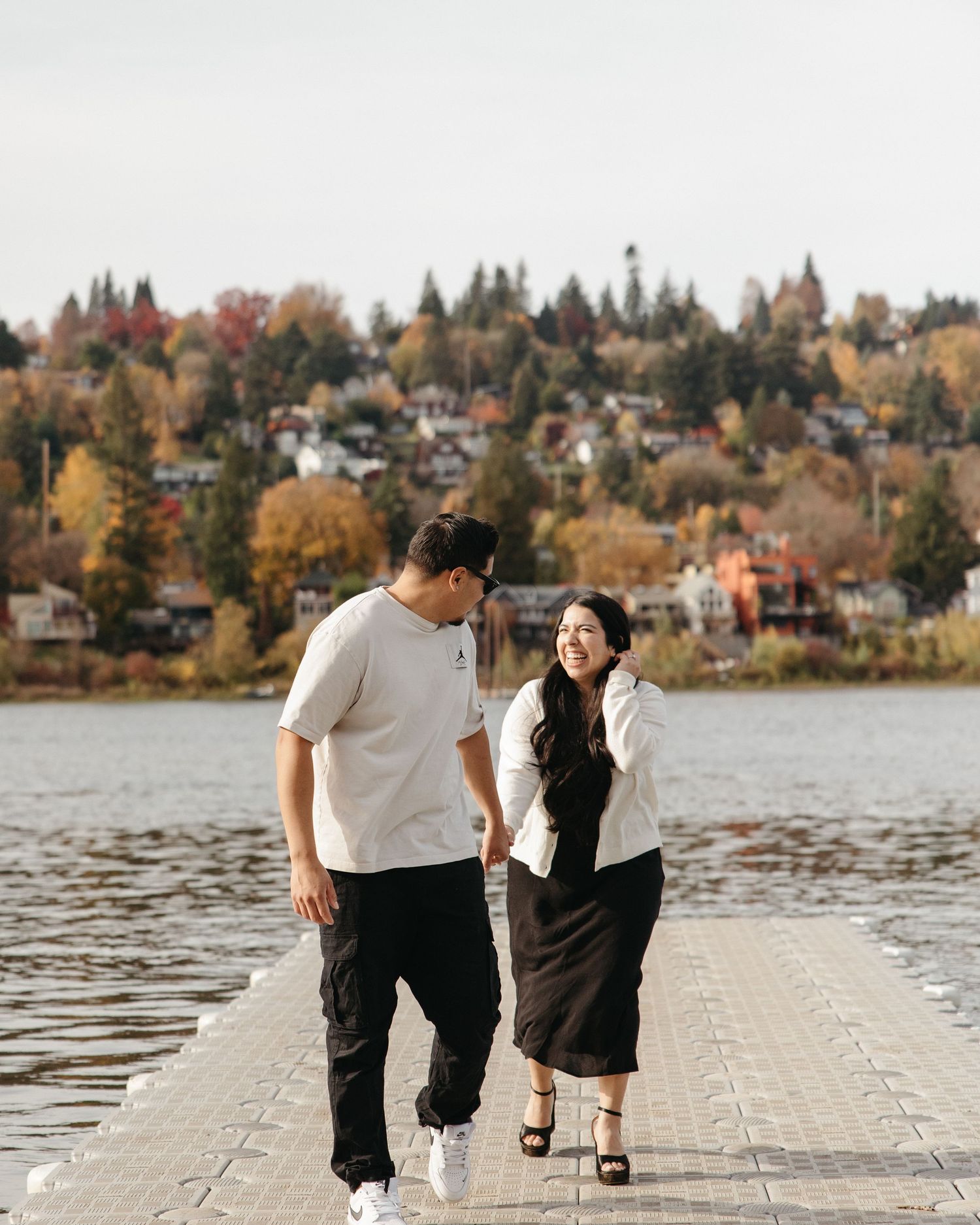 Family walking together on a wooden dock by a lake surrounded by autumn trees during sunset.
