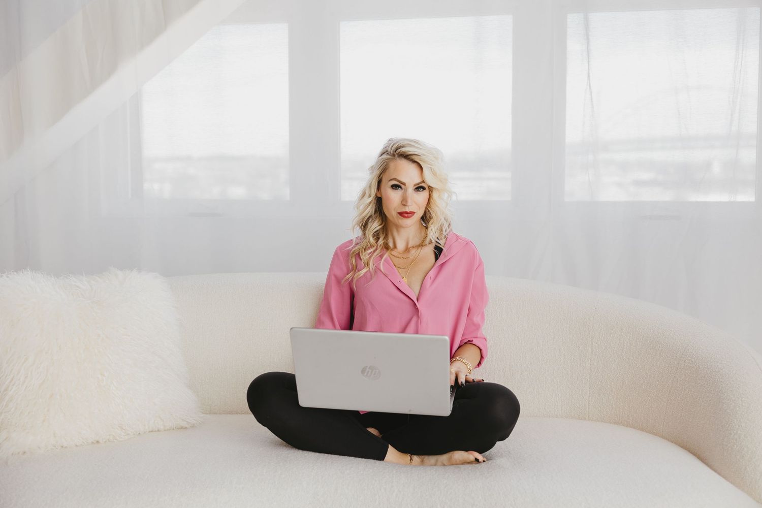 Woman in pink sweater sitting comfortably on white couch in bright modern living room setting.