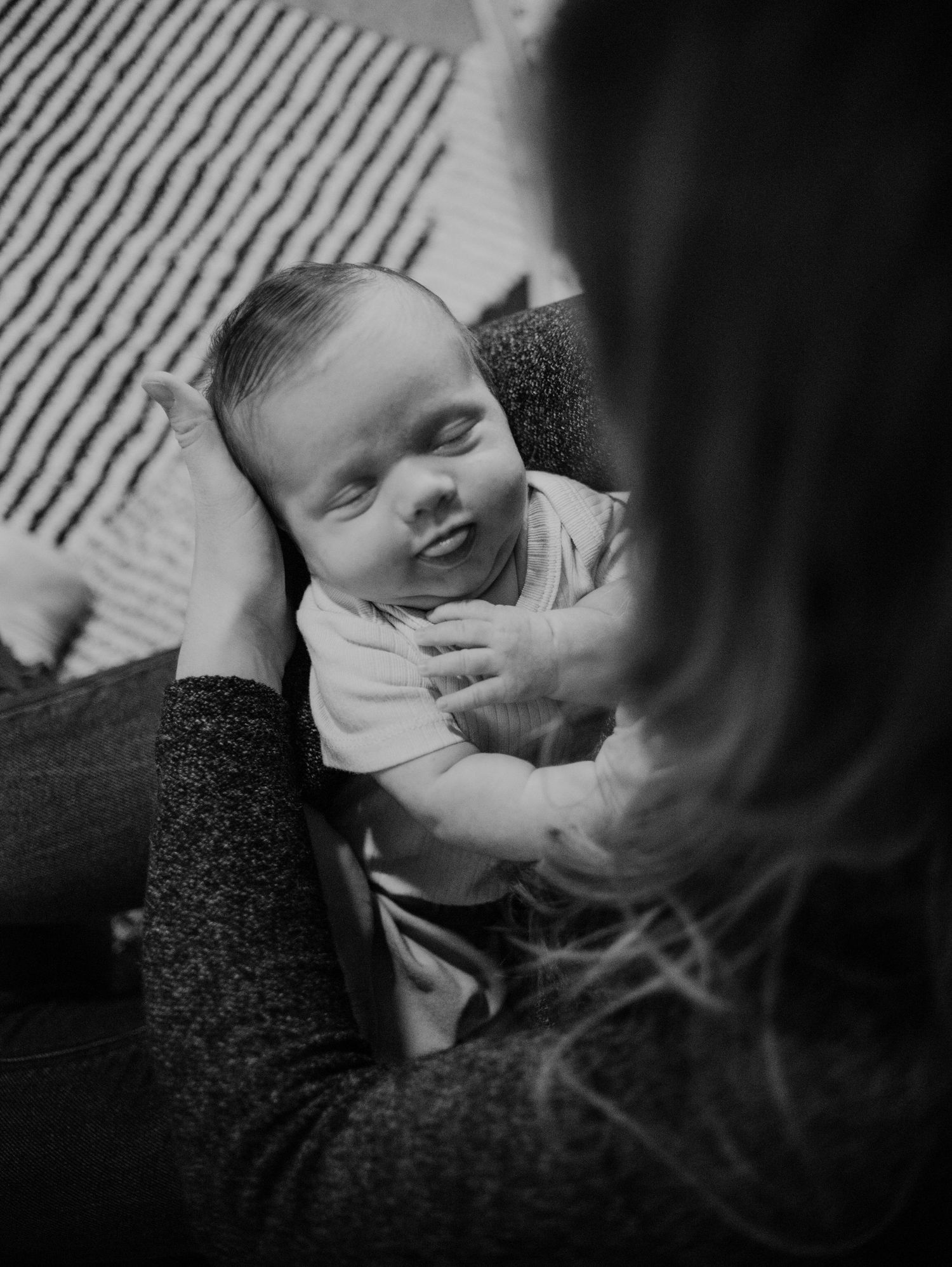 Black and white portrait of smiling baby lying on striped blanket.