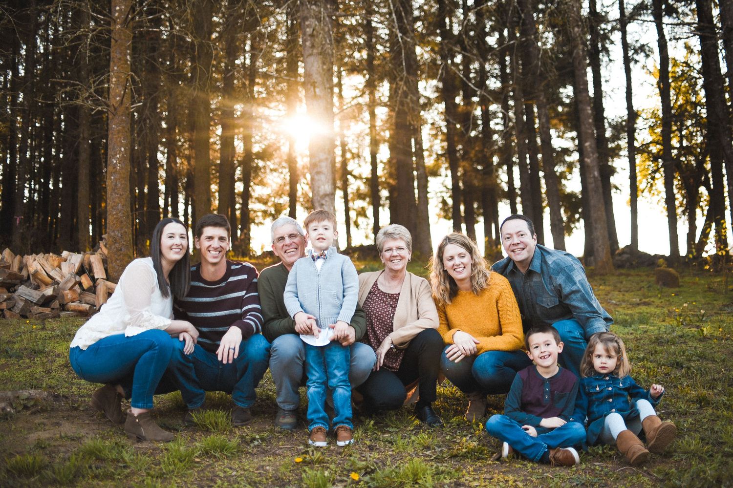 A multigenerational family gathers for a sunset portrait in a forest clearing with pine trees behind them.