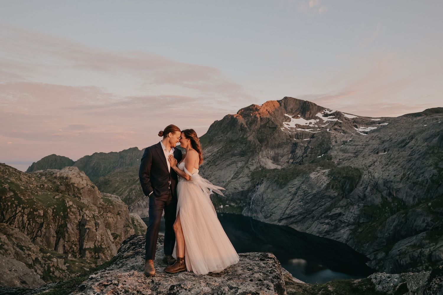 A couple shares an intimate moment on a mountaintop during sunset with a dramatic landscape backdrop.