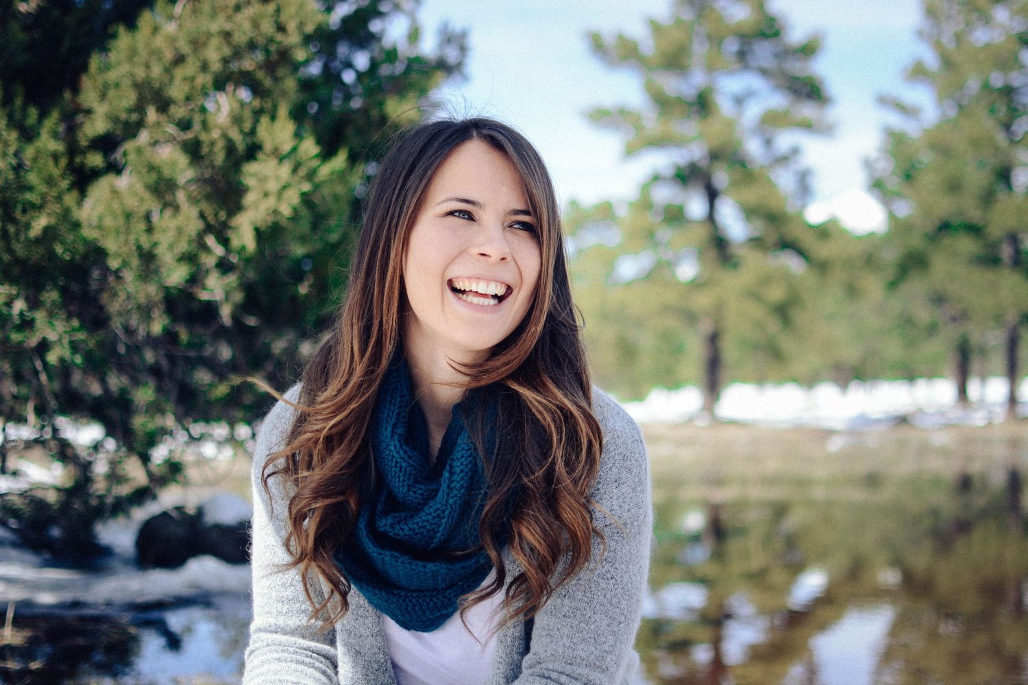 Joyful winter portrait with navy scarf and grey sweater against snowy landscape.