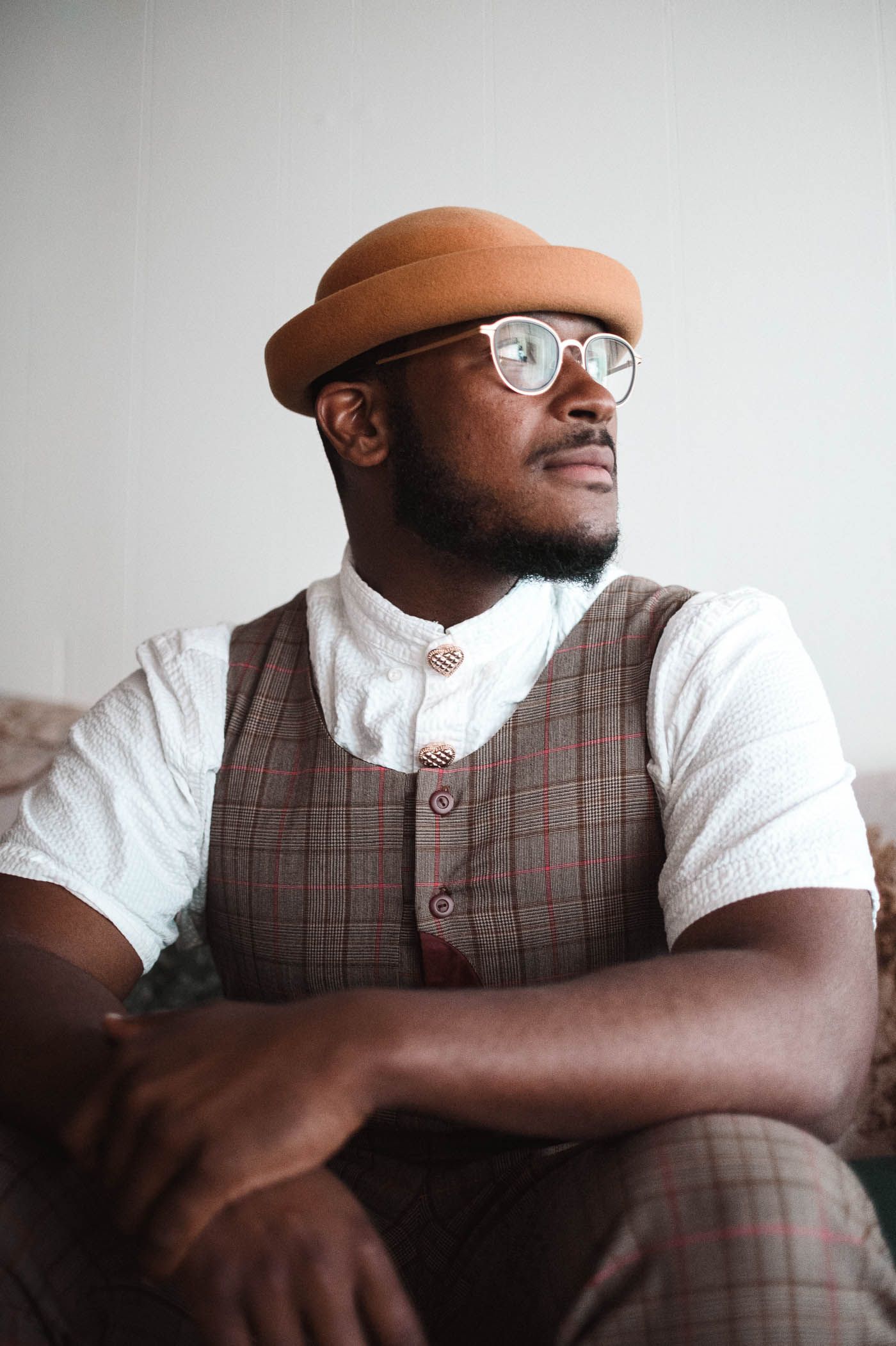 Stylish man in vintage attire with brown cap and glasses looking to the side.