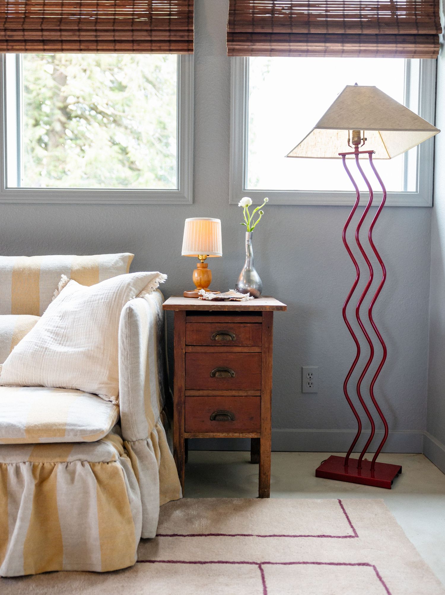 Living room corner with slipcovered sofa, wooden side table, and unique red wavy floor lamp.