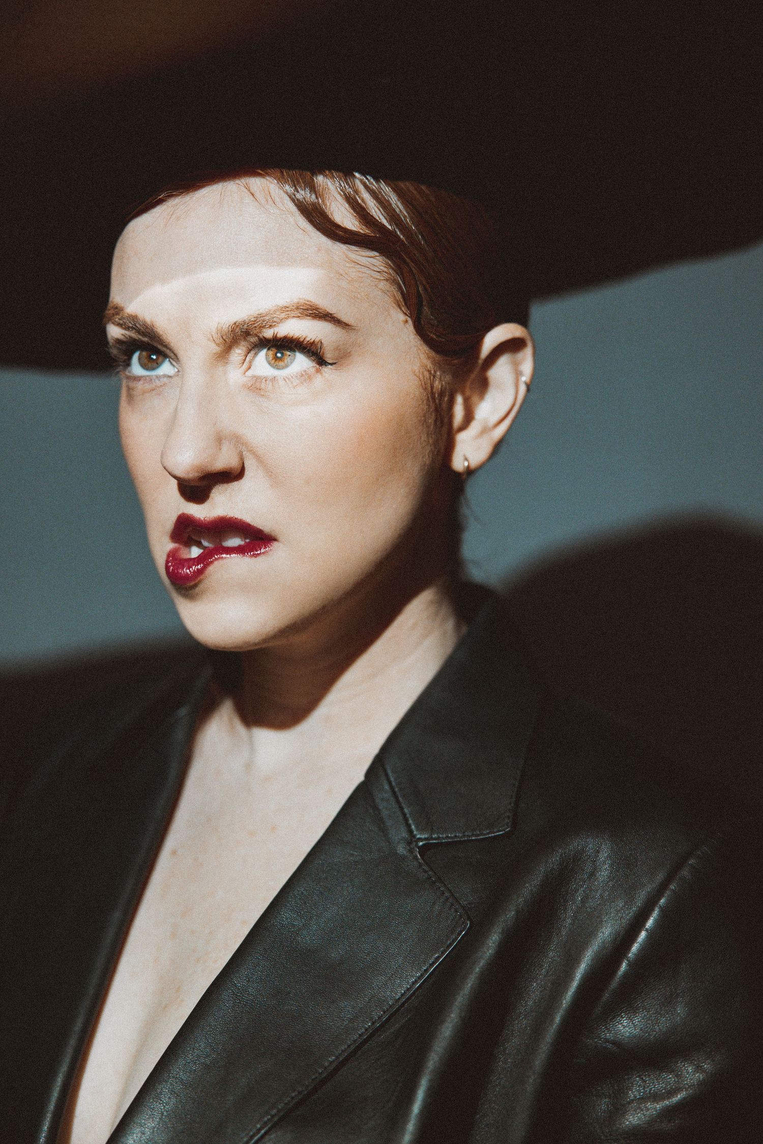 Close-up fashion portrait showing dramatic red lipstick and black leather jacket in moody lighting.