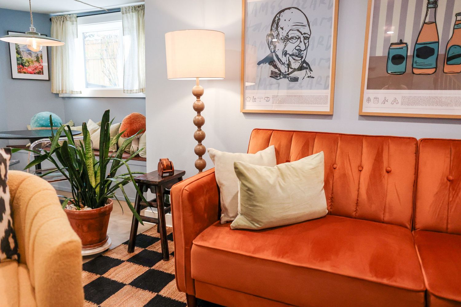 Mid-century modern living room with orange couch, checkerboard floor, and artistic wall prints.