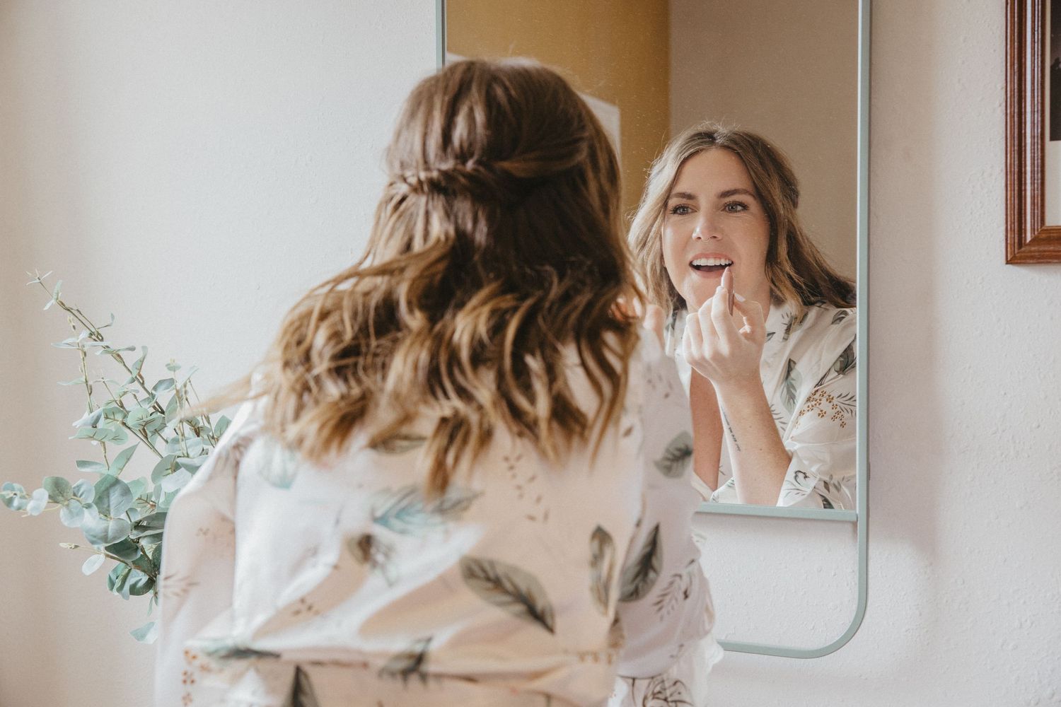 A joyful moment captured in a mirror reflection showing someone in a white robe getting ready for their wedding day.